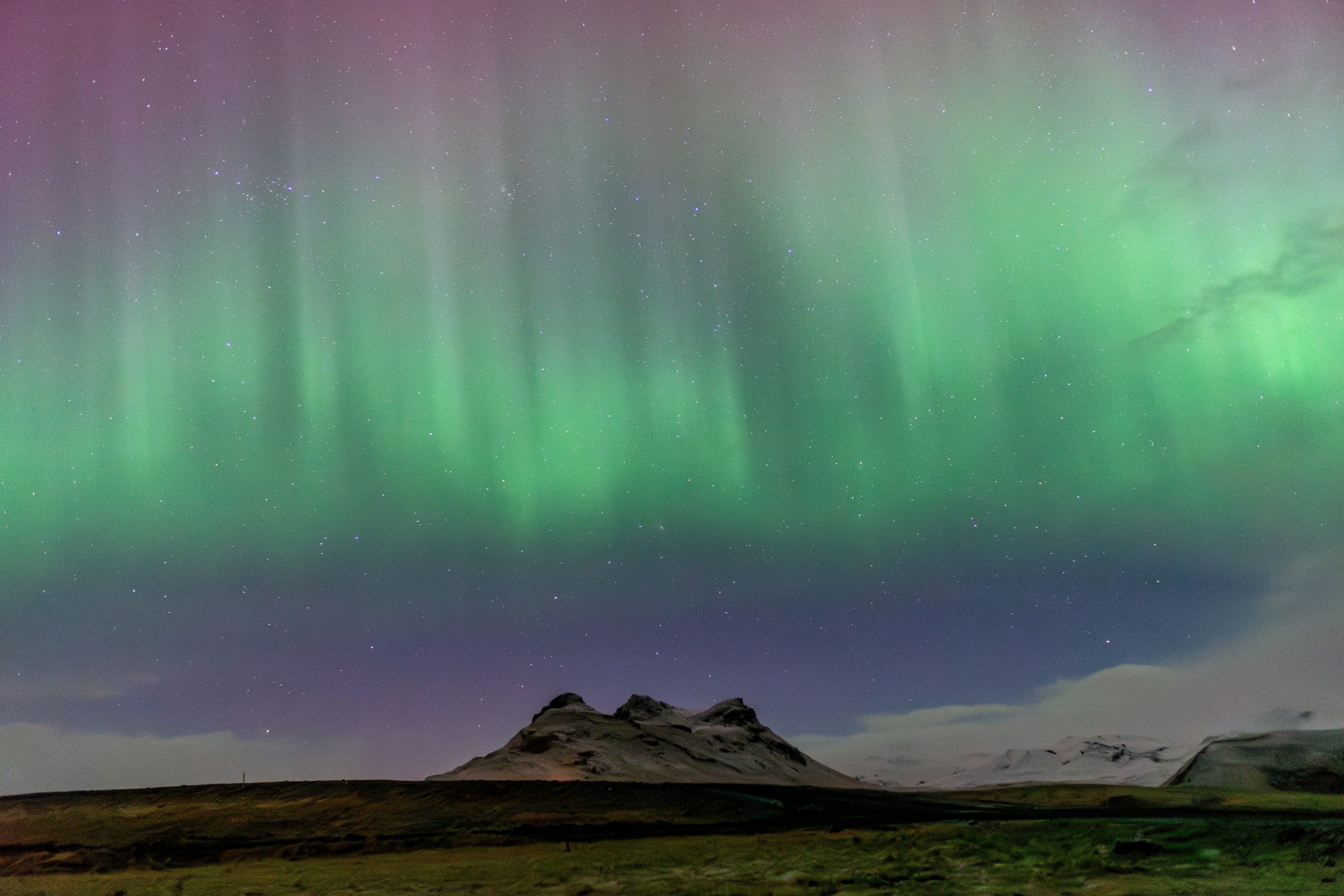 Aurora boreal verde y violeta sobre una montaña volcánica en la península de Snæfellsnes